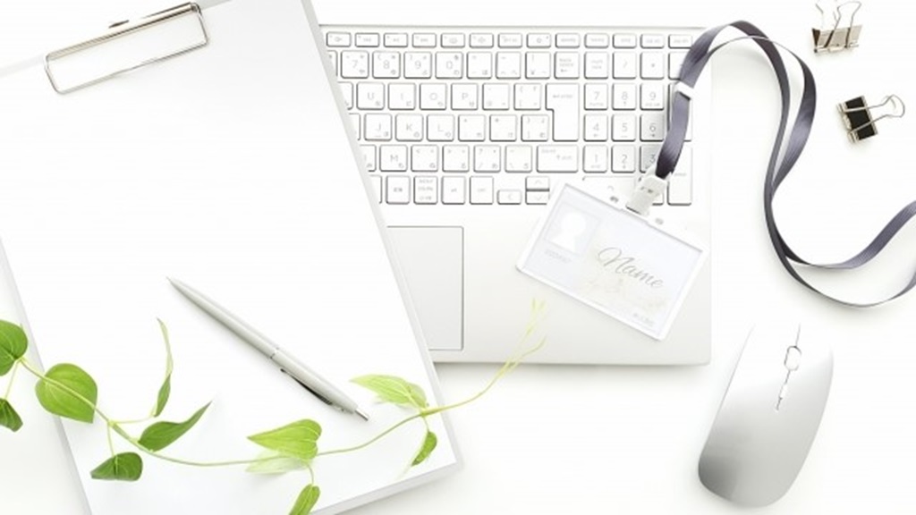 パソコン、Nameと書かれた社員証、紙、ボールペンが表象するアイデア出しの様子