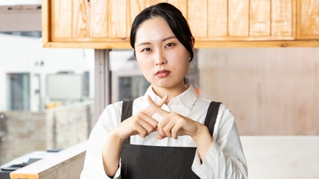 バツマークを指で作るカフェバイトの女性