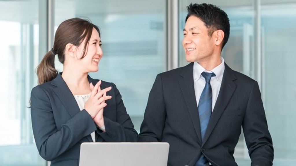 スーツを着た社員同士の男女が仕事中に談笑する様子
