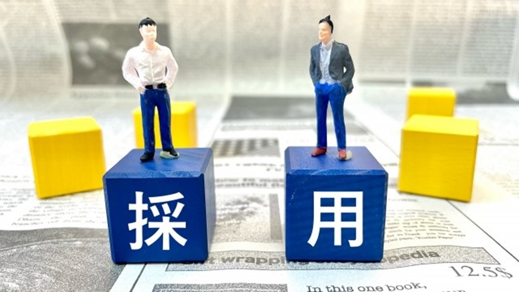 採用と書かれたサイコロブロックとそれに乗る社員のミニチュア
