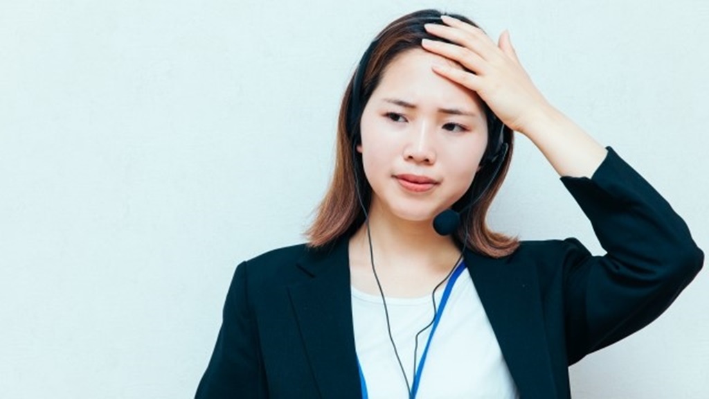 頭をおさえ眉間にしわを寄せる女性従業員