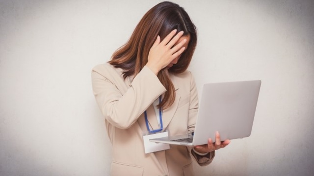 混乱を隠せず頭に手を当て悩みながら仕事をする女性従業員
