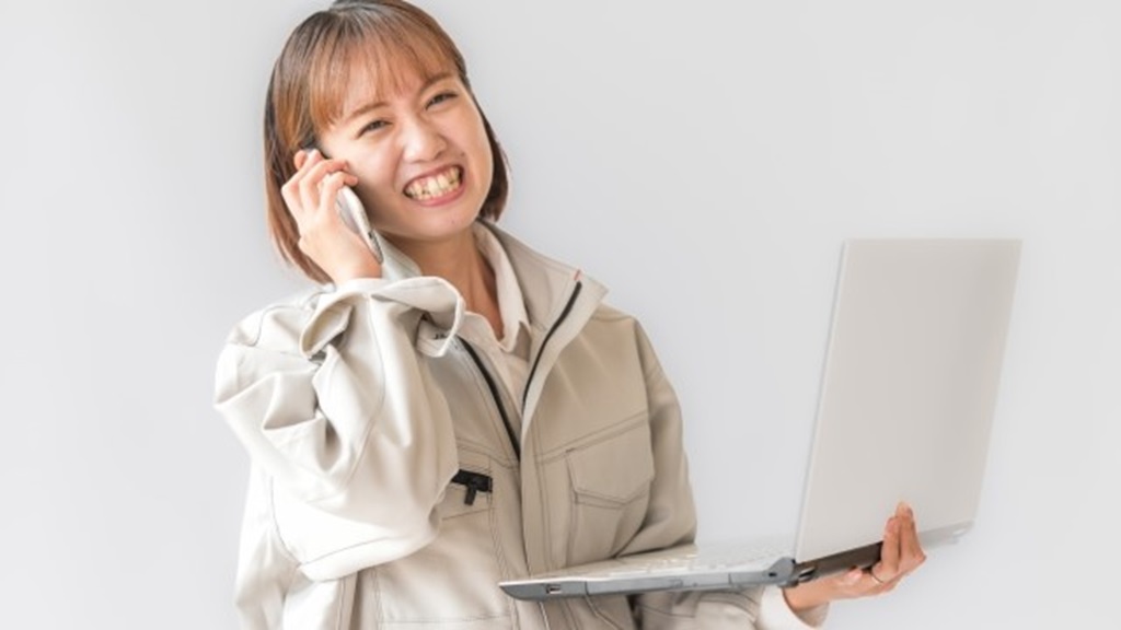 パソコンを持ちながら笑顔で電話をする作業服を着た従業員