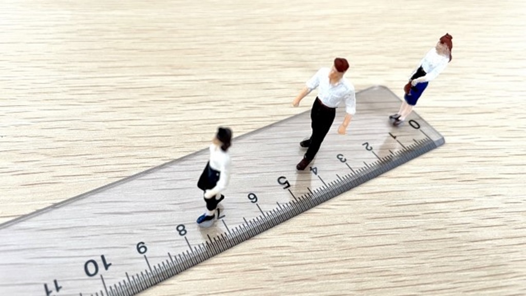 定規の上に立つ人員を示唆するビジネスパーソンの人形