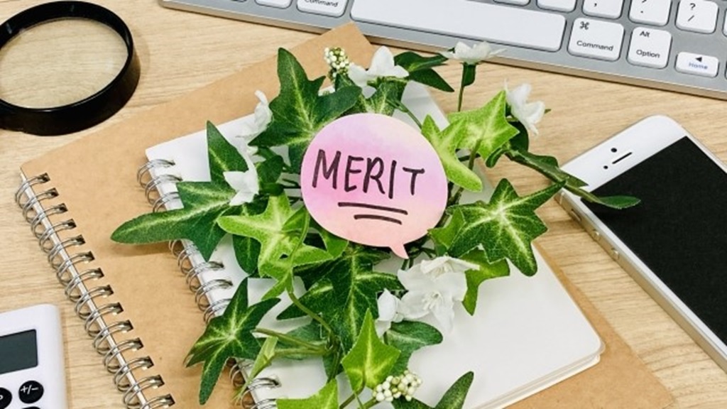 ノートと花の上に置かれたMERITと書かれた吹き出し