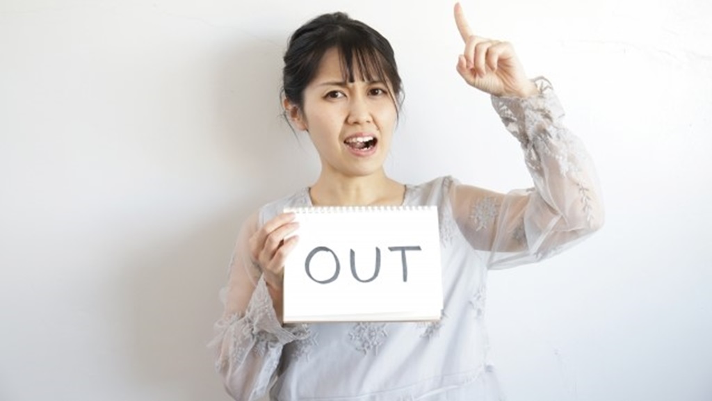 OUTと書かれた画用紙を持って怒りを表す女性